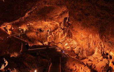 Cuevas de Mendukilo por dentro, con estalactitas y estalacmitas alumbradas con luces anaranjadas.