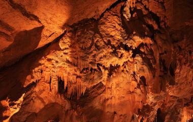 Cuevas de Mendukilo por dentro, con estalactitas y estalacmitas alumbradas con luces anaranjadas.