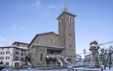 Iglesia de piedra con campanario puntiagudo en Erro, plaza nevada con escalinatas y construcciones tradicionales pirenaicas.