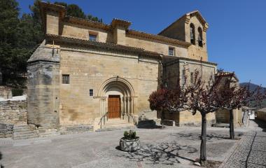 Iglesia de piedra arenisca con campanario en Eslava, plaza frontal con árboles y cielo despejado.