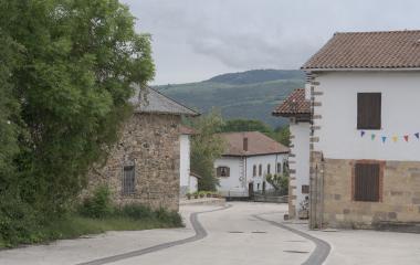 Calle de Esnoz con casas tradicionales de piedra y montaña boscosa al fondo.