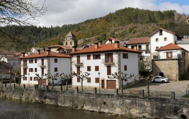 Casas blancas con tejados rojos junto al río en Esparza de Salazar, con iglesia y montaña boscosa al fondo.