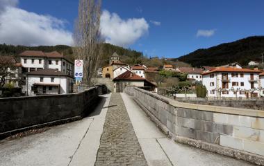 Puente de piedra y arquitectura tradicional en Esparza de Salazar, pueblo pirenaico con casas de tejado rojo y bosque de fondo.