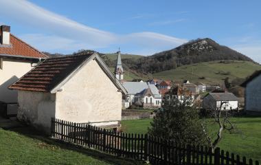 Iglesia con campanario y casas tradicionales de piedra en Garralda, rodeadas de prados y montes verdes del Pirineo.