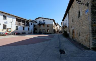 Plaza central de Ibargoiti con casas de piedra y fachadas blancas bajo cielo despejado.