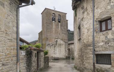 Iglesia de piedra con torre campanario en el pueblo de Ilurdoz, Pirineo navarro, flanqueada por arquitectura tradicional de piedra.