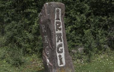 Piedra con inscripción de nombre del pueblo con fondo de vegetación en Iragi, Pirineo navarro.