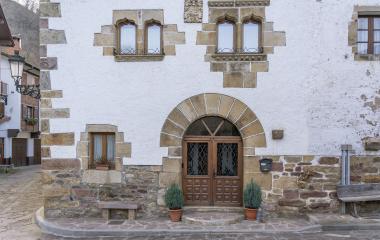 Fachada blanca con ventanales condetalles, porton de piedra enrejada y decoraciones tradicionales vascas en Ituren.