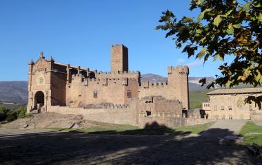 Castillo de Javier con torres almenadas, iglesia y montes al fondo en día soleado.