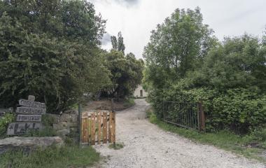 Entrada a Lacabe con cartel de bienvenida trilingüe, camino de tierra y vegetación frondosa.