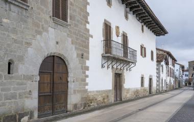 Calle empedrada de Larrasoaña con casas de piedra blanca, portada románica y balcón de hierro forjado.