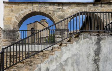 Escaleras de piedra con barandilla metálica moderna en Leache, enmarcando arco de paso hacia pueblo.