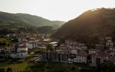 Vista aérea de Leitza con casas de tejado rojo, rodeadas de montes boscosos y prados verdes.