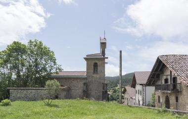 Iglesia de piedra cen Lenaroz, Pirineo navarro, rodeada de caseríos tradicionales y prado verde.