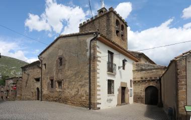 Iglesia rural de Liédena con torre campanario de piedra asoma detrás de casas de piedra.