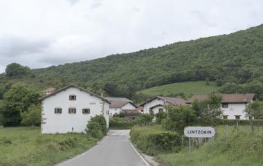 Entrada al pueblo de Lintzoain en el Pirineo navarro con caseríos blancos tradicionales rodeados de bosque y prados verdes.