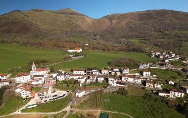 Vista aerea de Luzaide-Valcarlos con iglesia, casas tradicionales y montanas boscosas del valle pirenaico.