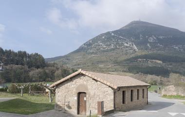 Edificio de piedra en Higa de Monreal con montaña boscosa al fondo y prado verde.