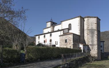 Iglesia parroquial con campanario de piedra, rodeada de edificios y elementos religiosos en Narbarte.