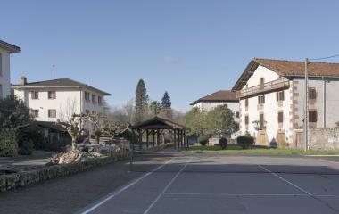 Plaza de pueblo con pista de tenis y casas vascas blancas alrededor en Oieregi.