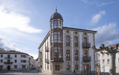 Edificio singular con torre cupulada y fachada de piedra en Olazti, rodeada de arquitectura tradiconal.