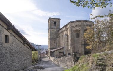 Iglesia de piedra con campanario en Olazti, rodeada de casas tradicionales y vegetación en ladera.