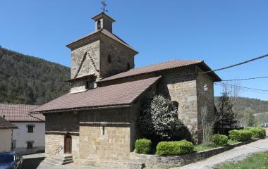 Iglesia de piedra con campanario en Oronz, rodeada de vegetación.