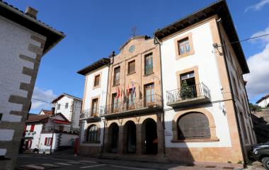 Ayuntamiento de piedra arenisca y blanco en Oroz-Betelu con reloj, balcones y bandera, flanqueado por casas tradicionales pirenaicas.