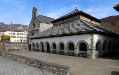 Iglesia con pórtico de arcos de piedra y tejado de pizarra en Orreaga, rodeada de arquitectura tradicional pirenaica.