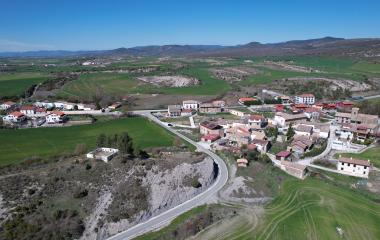 Vista aerea del pueblo de Romanzado con casas dispersas, campos verdes y montana al fondo en el prepirineo.