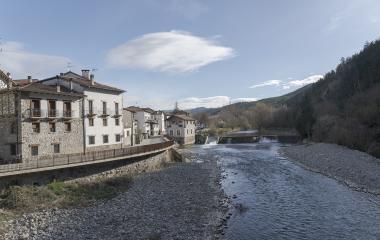 Río Esca fluyendo junto a casas de piedra en Burgui, Valle de Roncal, con bosque pirenaico al fondo.