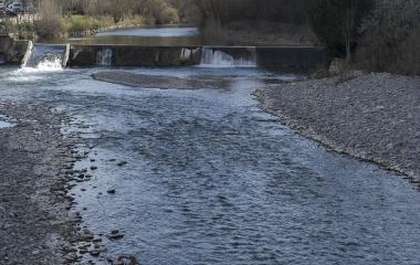 Río Esca en Burgui con presa y vegetación en primavera temprana, aguas claras y gravas.