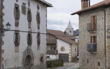 Calle empedrada del pueblo de Saldias con casas de arquitectura tradicional vasca de paredes blancas y una iglesia al fondo.