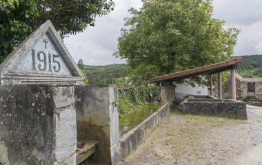 Lavadero de 1915 en Sarasibar, con fuente, canal y construccion cubierta rodeada de vegetacion.