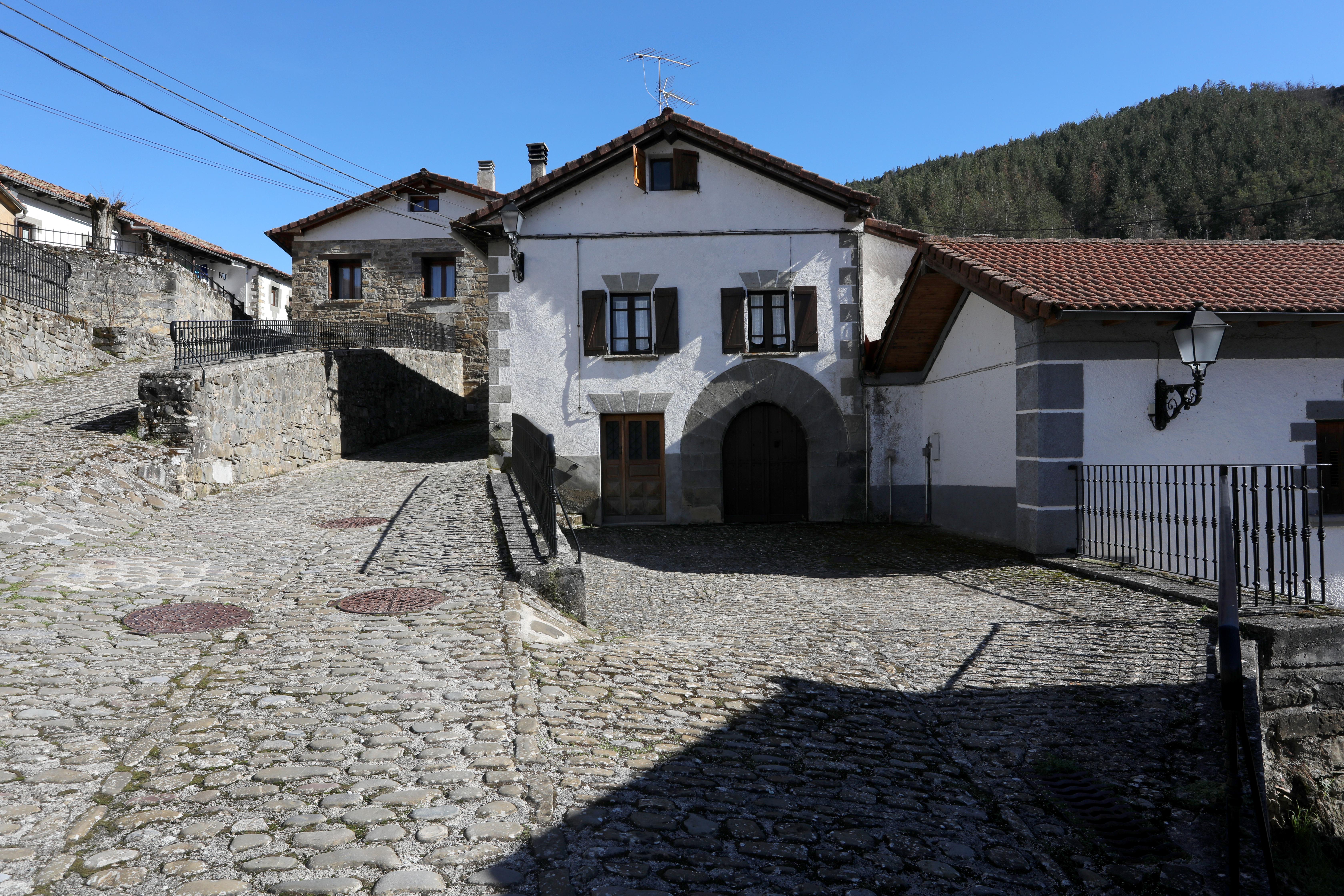 Calle empedrada de Sarries con casas de piedra blanca y tejado tradicional pirenaico, bosque al fondo.