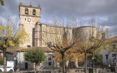Iglesia de piedra con campanario en plaza de Uharte Arakil, rodeada de árboles y arquitectura tradicional.