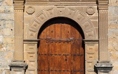 Portada de piedra con puerta de madera en Urraul Bajo, flanqueada por columnas estriadas y decoración geométrica.
