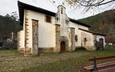 Iglesia de piedra y blanca con campanario en Uztarroz, rodeada de bosque pirenaico en otoño.
