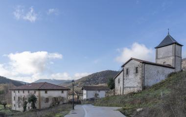 Vista de lo que parece el final del pueblo de Anue con casas y una iglesia, rodeada de montes.