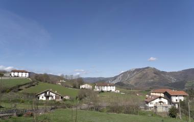 Casas dispersas en el Valle de Araitz con montes al fondo y prados verdes de primavera bajo cielo despejado.