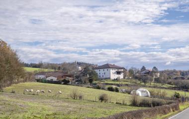 Casas tradicionales y prados verdes en el valle de Atez, con ovejas pastando y cielo nublado.