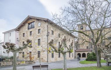 Ayuntamiento de Ziordia, edificio de piedra tradicional, iglesia al fondo y árboles desnudos en primavera.
