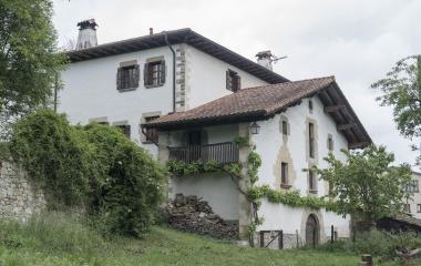 Casa tradicional de piedra y cal blanca con balconada de madera en Zuriain, con prado verde y vegetacion al lado.